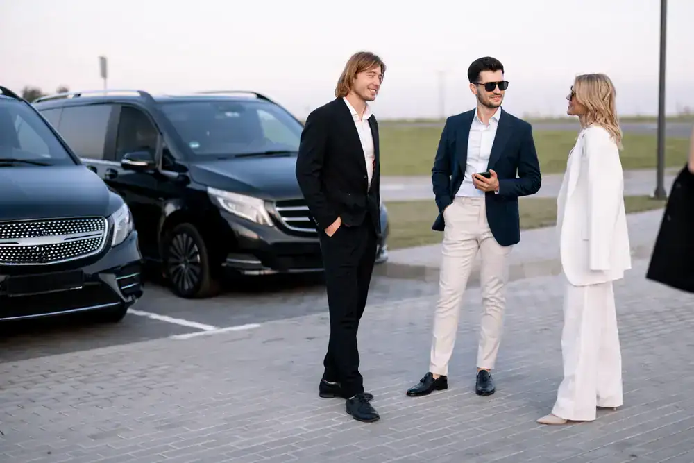 Three stylishly dressed people chat in a parking lot beside two sleek black vehicles, suggesting a formal, upscale scene—perfect for those seeking premium black car service Newark, NJ for special occasions or professional events.