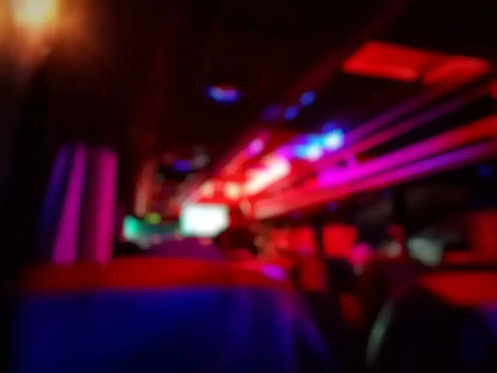 Blurry image of a bus interior at night, with vibrant red, pink, purple, and blue lights illuminating the ceiling and seats—like the colorful ambiance you'd see after booking a black car service in Newark, NJ.